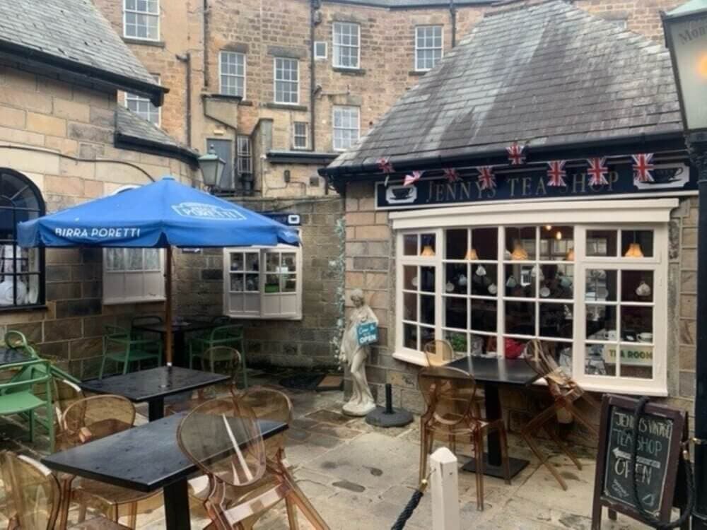 A quaint outdoor seating area of a tea shop with British flags, wooden chairs, and an umbrella-covered table. - Home Instead