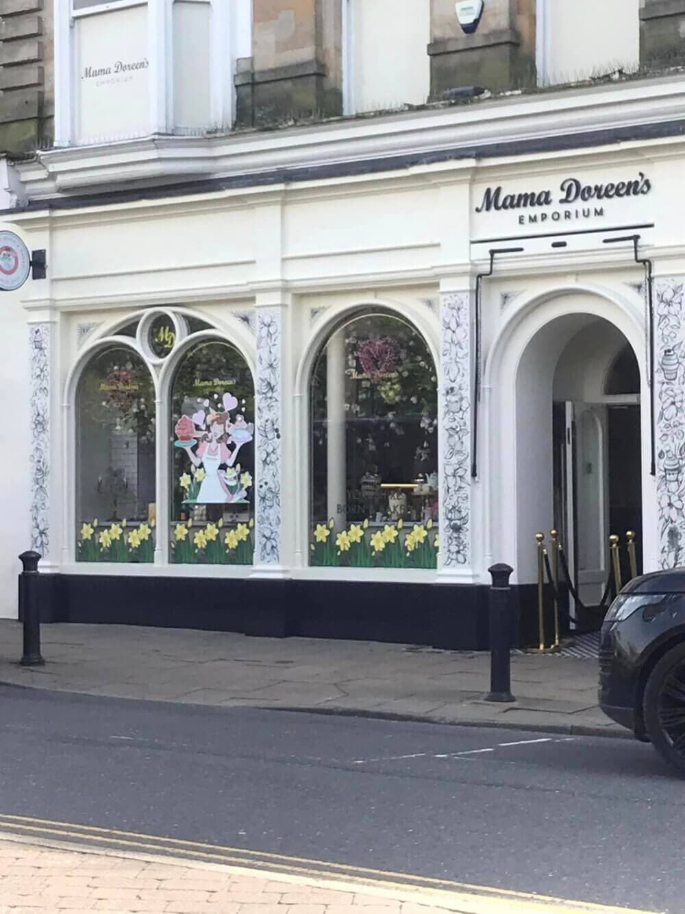 Exterior of Mama Doreen's Emporium with decorative window displays and yellow flowers in front. - Home Instead