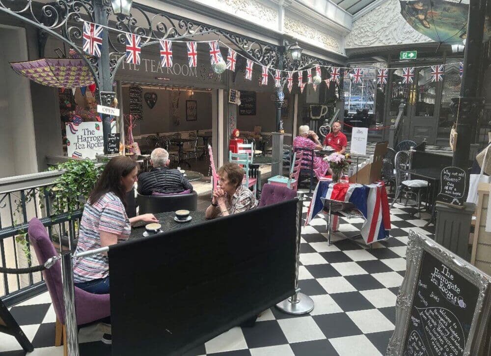 People sitting at tables in a vintage-style tearoom adorned with British flags and eclectic decor. - Home Instead