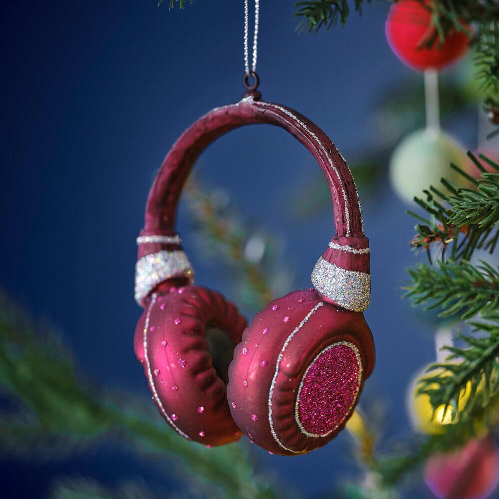 Red and glittery headphone ornament hanging on a Christmas tree with a blurred background. - Home Instead