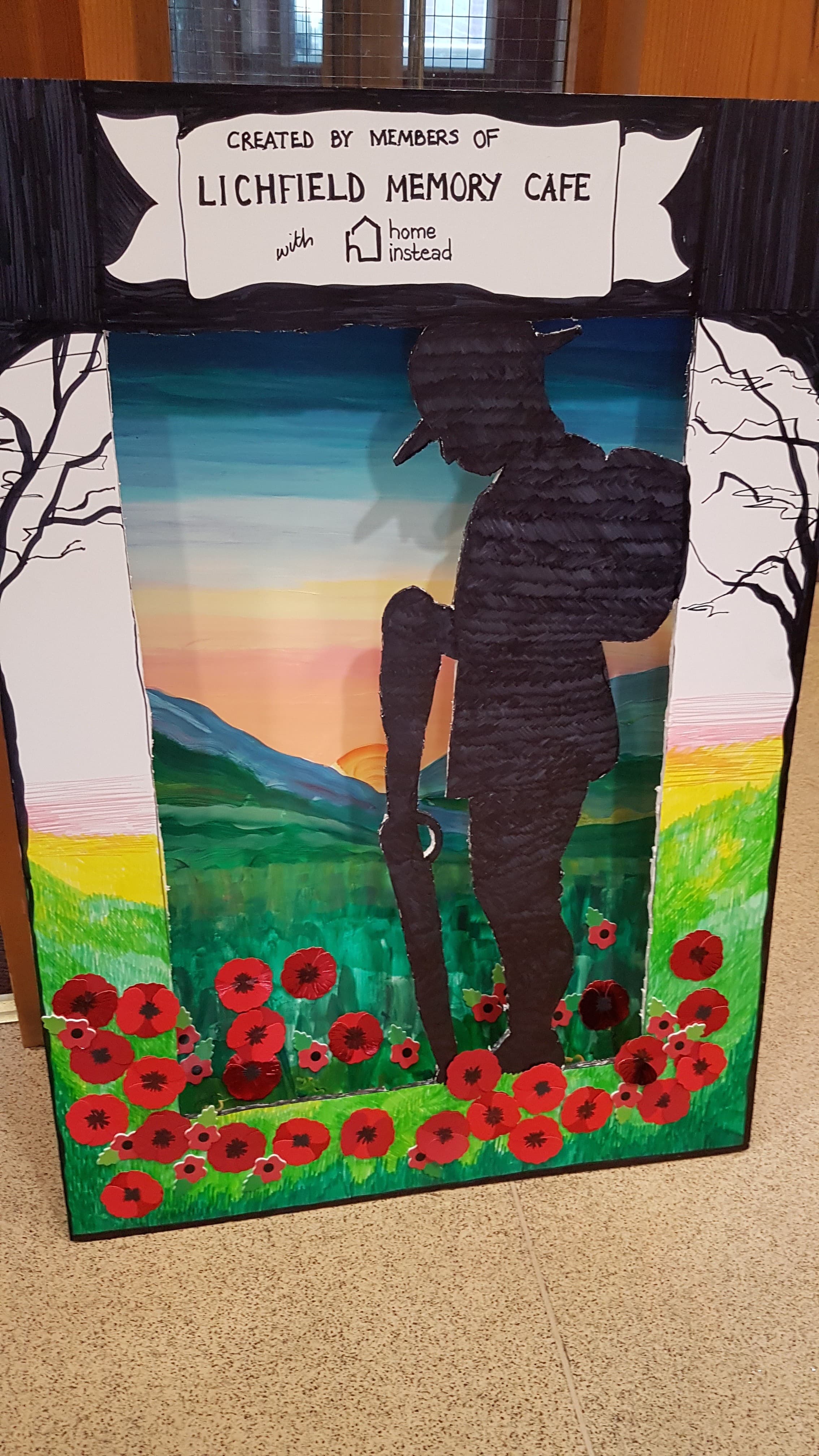 Silhouette of a soldier among red poppies, with a sunset background and sign for Lichfield Memory Cafe. - Home Instead