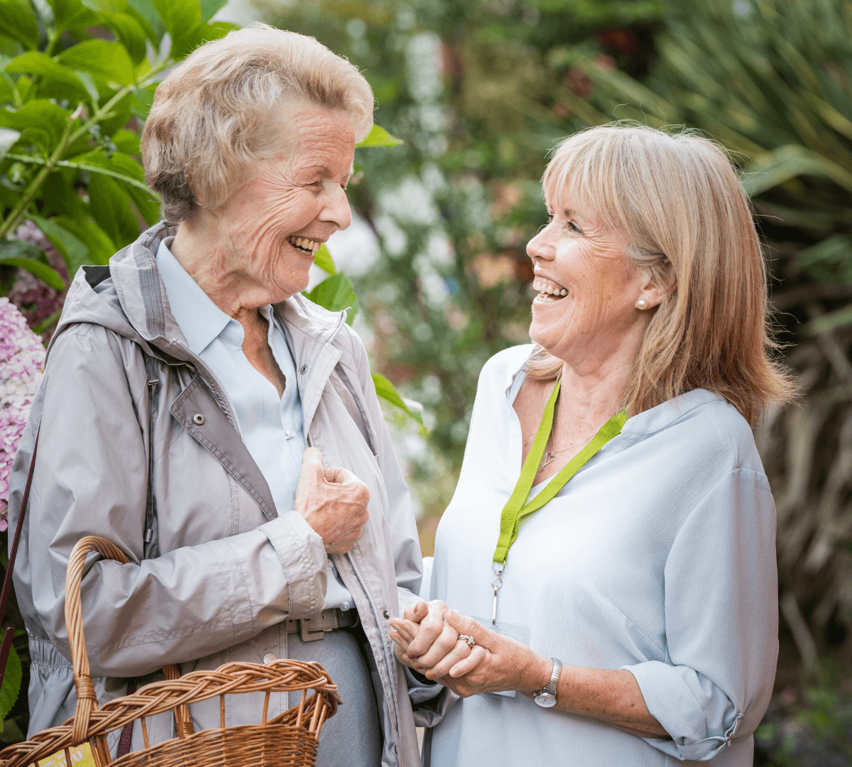 An older female adult with grey hair happy and smiling while bringing a basket with her younger female carer beside her