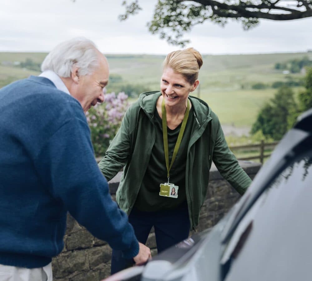 An older male adult with white hair riding a car with his younger female carer