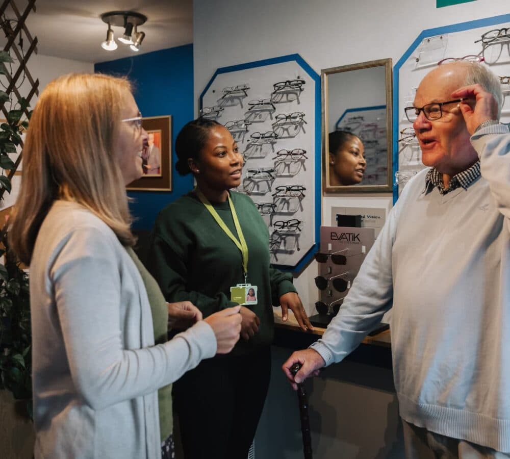 An older male adult smiling while wearing glasses and chatting with two women