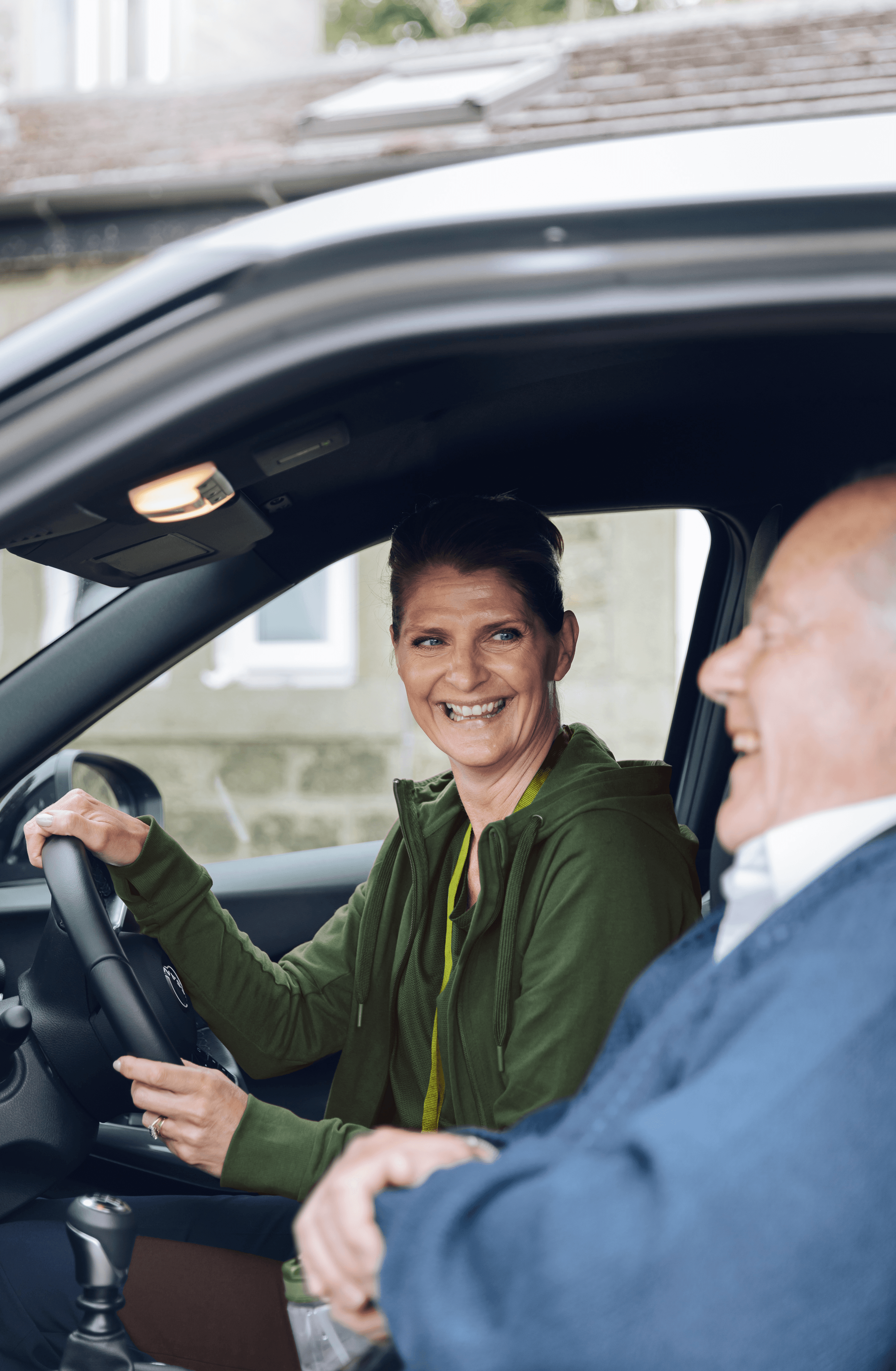 Smiling woman in the driver's seat and an older man in the passenger seat, both inside a car. - Home Instead