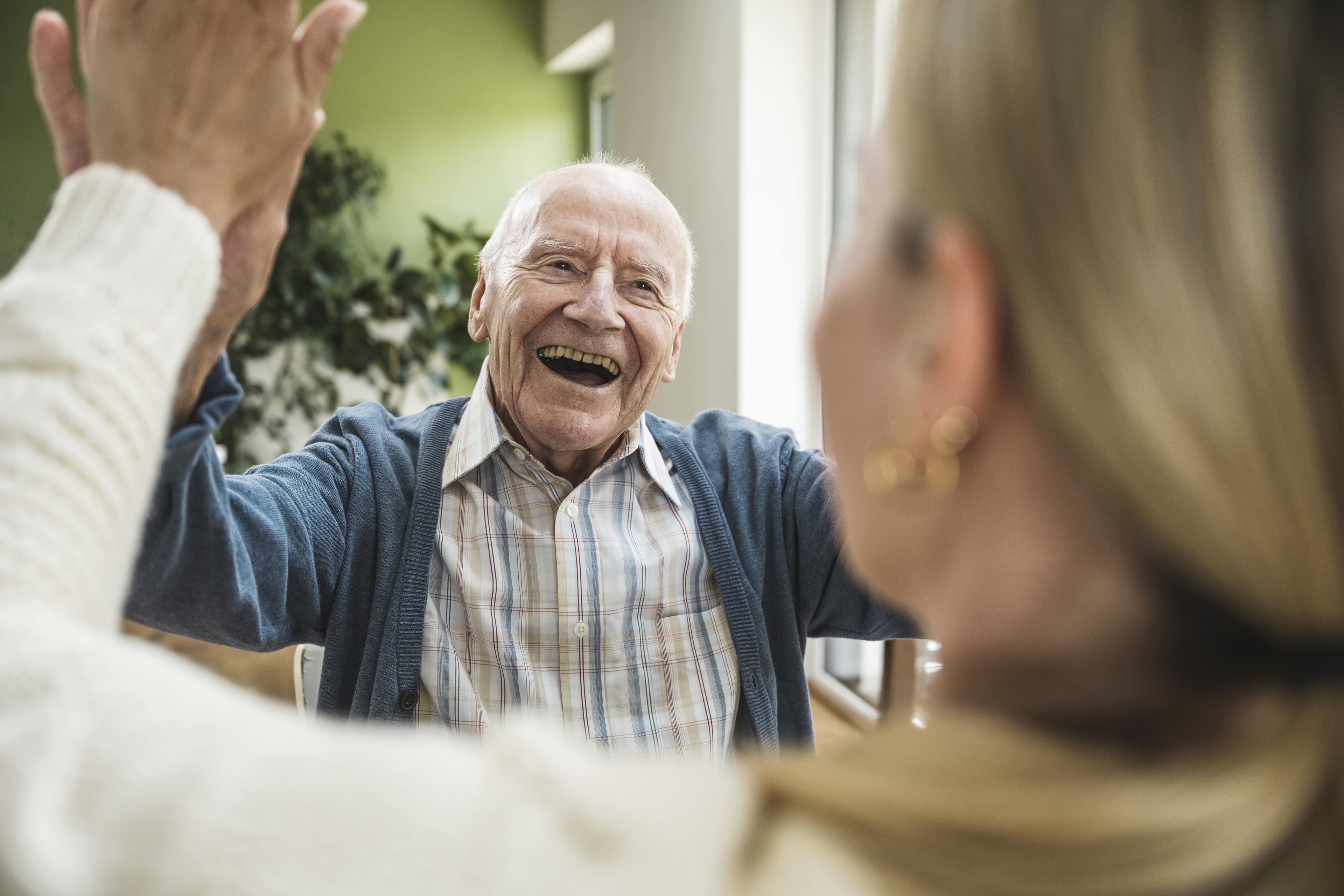 Smiling elderly man gives a high five to a woman indoors, both appearing happy and joyful. - Home Instead