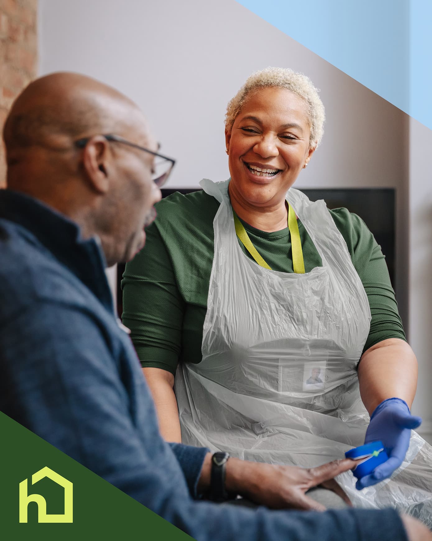 Smiling caregiver in gloves talks with an older man at home; a house icon is in the corner. - Home Instead