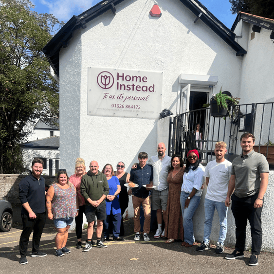 A group of people standing outside a white building with a sign that reads "Home Instead. - Home Instead