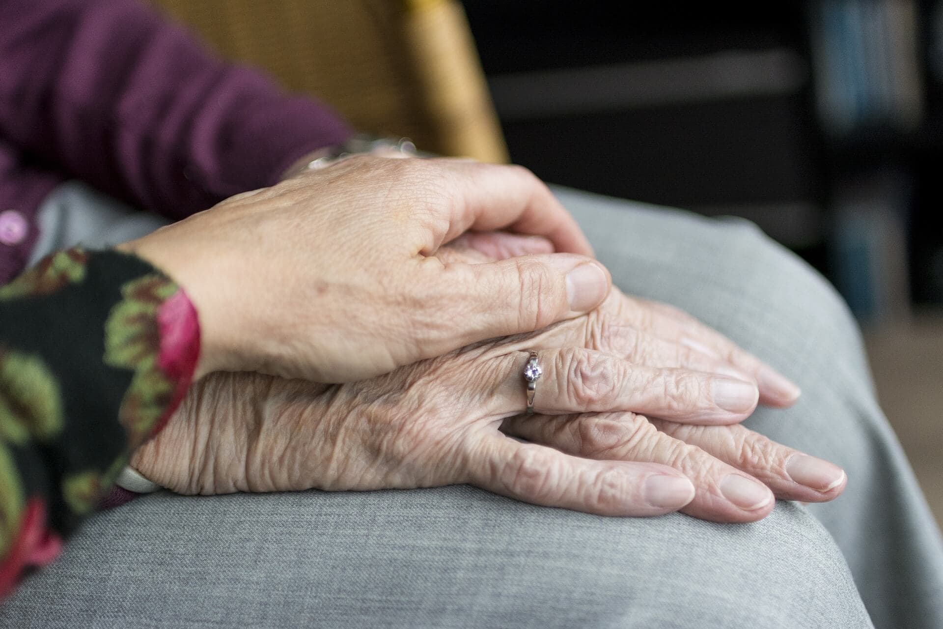 An elderly person's hand with a ring is gently held by another person's hand. - Home Instead