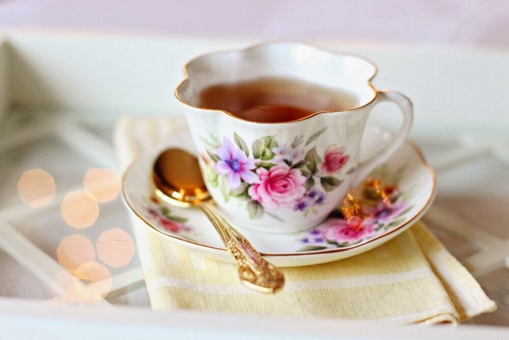 Elegant teacup with floral design filled with tea, on a matching saucer with a gold spoon and a yellow cloth napkin. - Home Instead