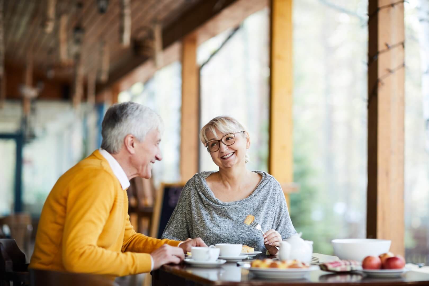 Older couple smiling and enjoying a meal together at a bright, cosy café with large windows. - Home Instead Southampton