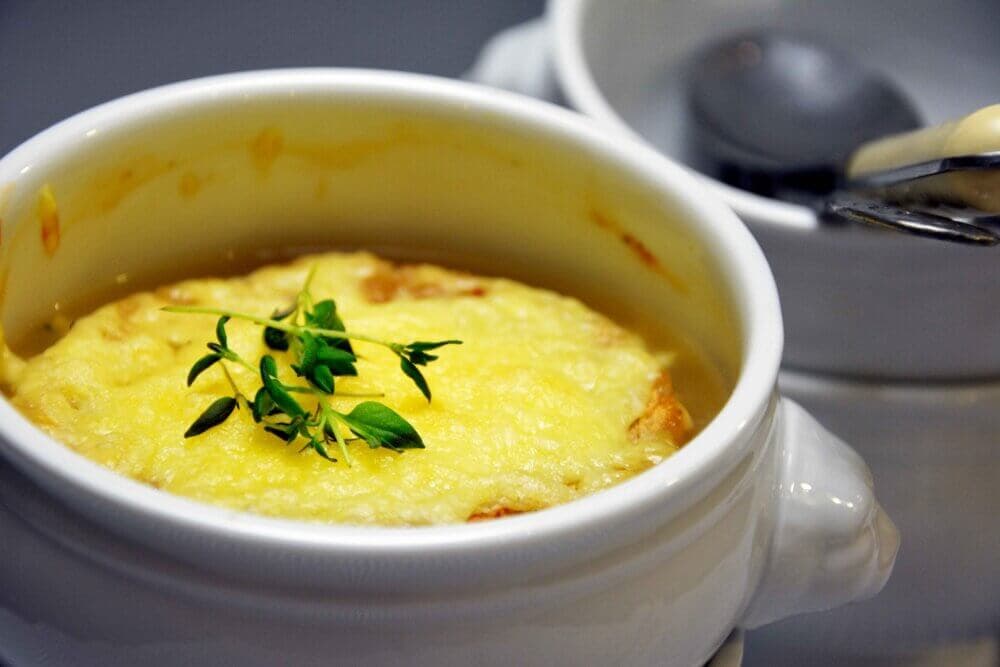 A bowl of French onion soup topped with melted cheese and garnished with fresh herbs. - Home Instead