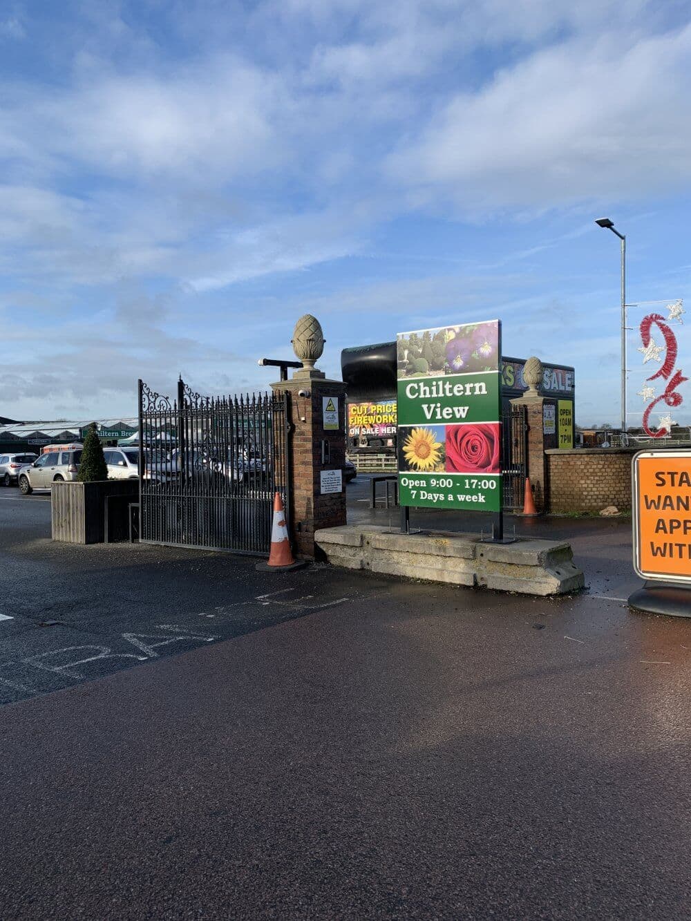 Entrance to Chiltern View shop with open gates and signage, surrounded by parked cars under a partly cloudy sky. - Home Instead