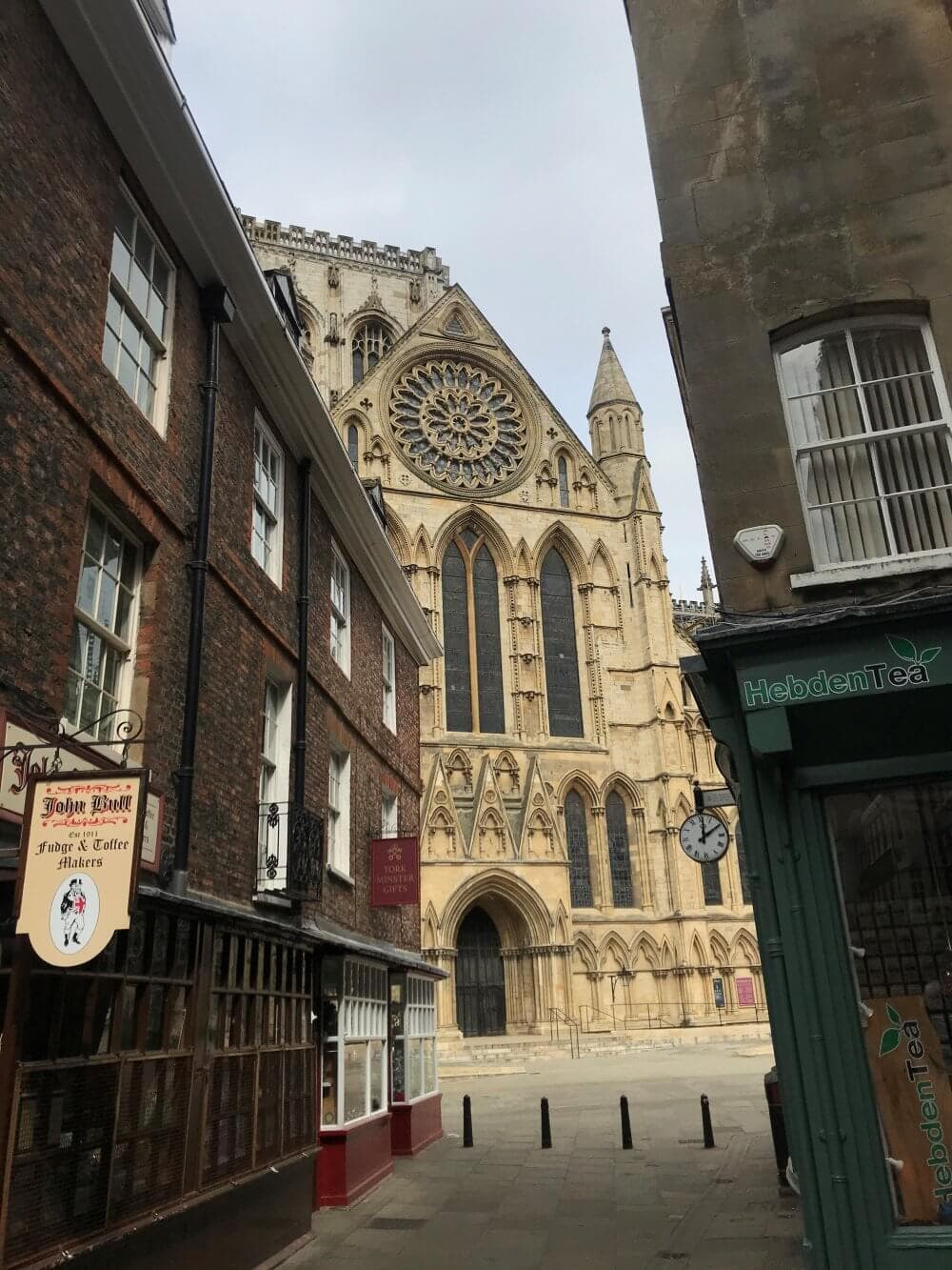 Narrow street with shops leading to a large, intricate cathedral with a circular stained-glass window. - Home Instead