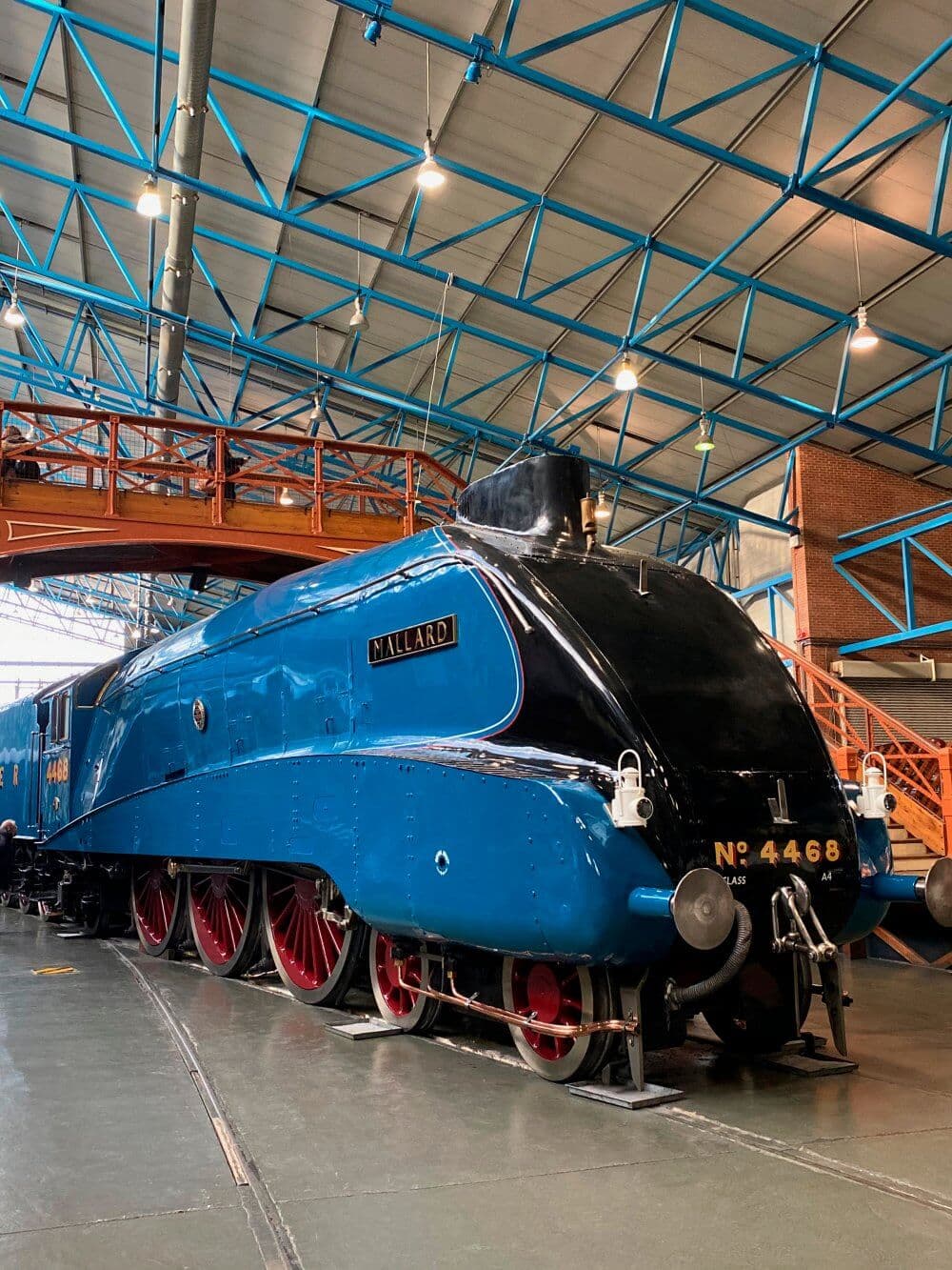 A blue steam locomotive named "Mallard" on display in an indoor museum with a high ceiling and metal beams. - Home Instead
