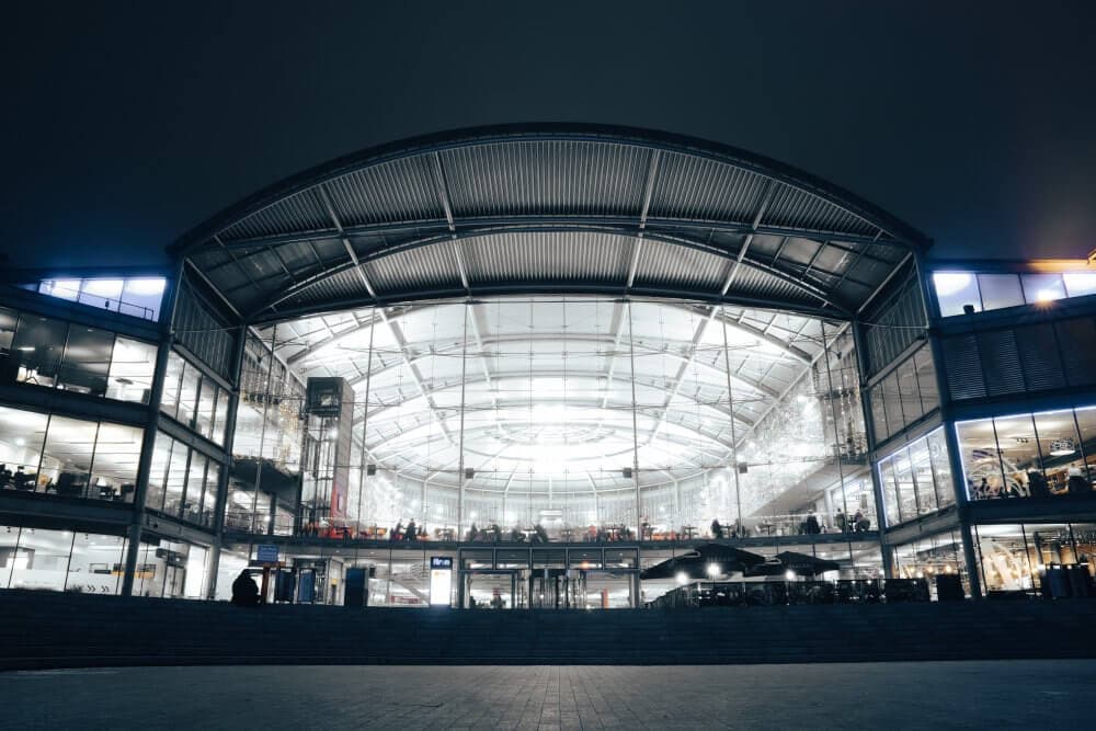 Modern building with a large, illuminated glass entrance and visible interior walkways, photographed at night. - Home Instead