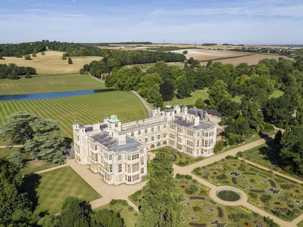 Aerial view of a large historic mansion with formal gardens, surrounded by lush greenery and fields. - Home Instead