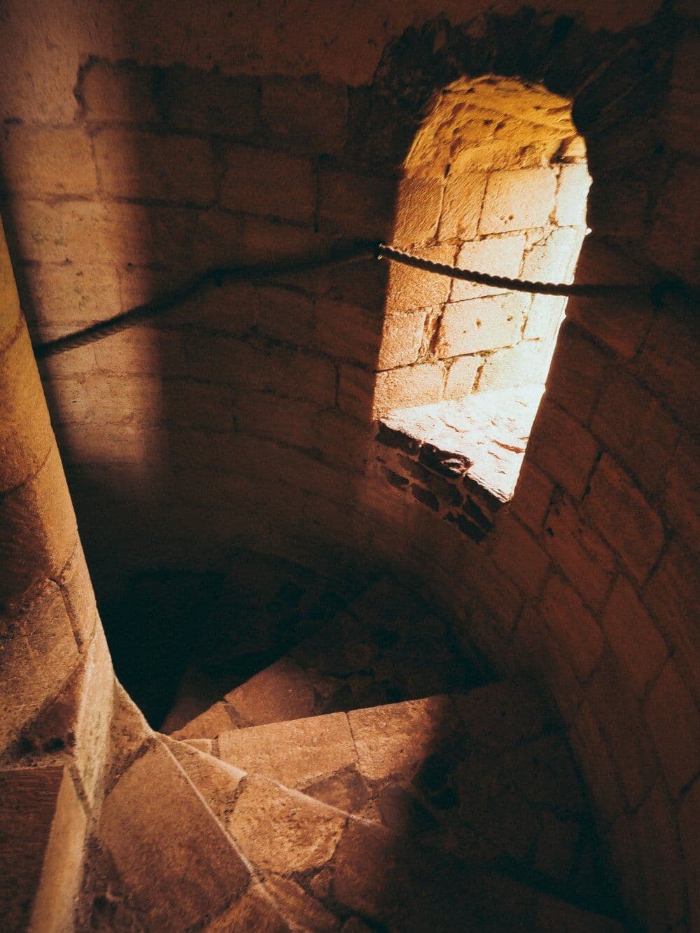 Spiral stone staircase with light streaming through a window in an old brick wall. - Home Instead