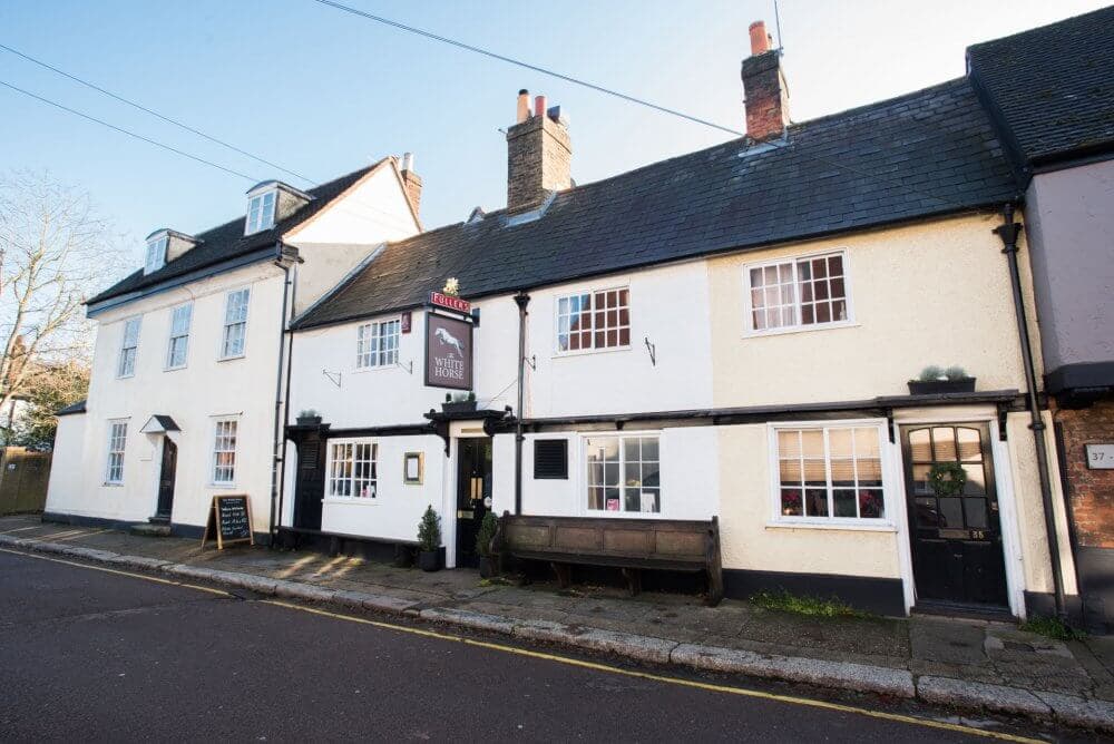 Historic white building with sign reading "The White Horse" on a quiet street with yellow curb and sidewalk benches. - Home Instead