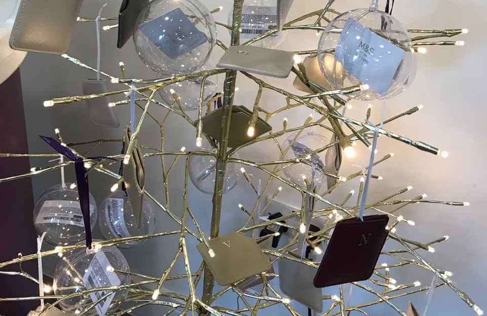 A gold tree-shaped holiday decoration with lights and clear ornaments, each holding a small card inside. - Home Instead