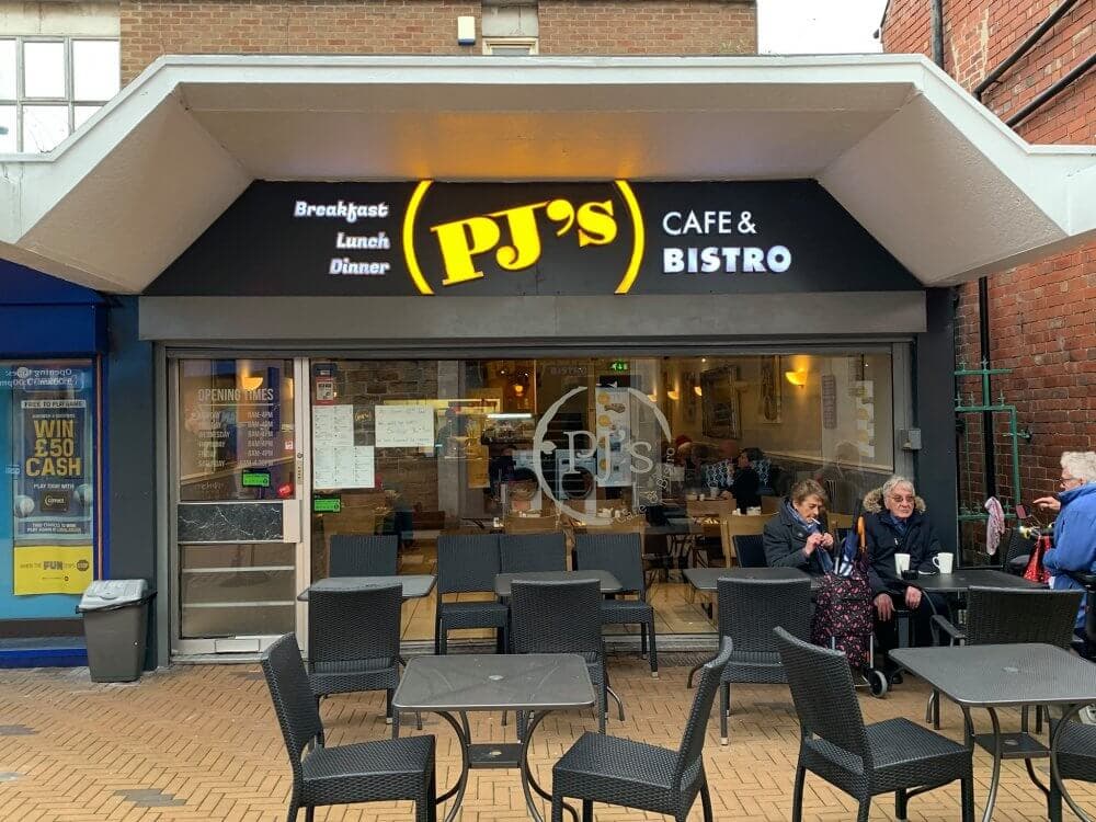 Outdoor view of PJ's Cafe & Bistro with customers seated at tables, and the sign promoting breakfast, lunch, and dinner. - Home Instead