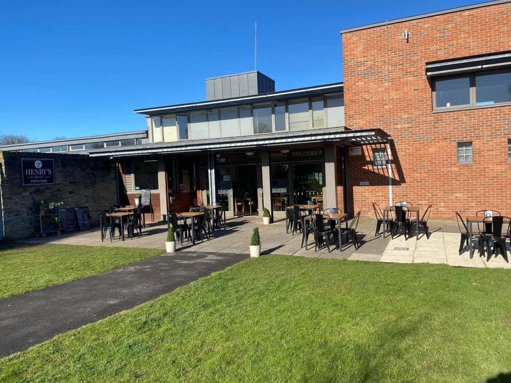Outdoor seating area of a brick cafe with tables, chairs, and a sign that reads "Henry's Cafe. - Home Instead