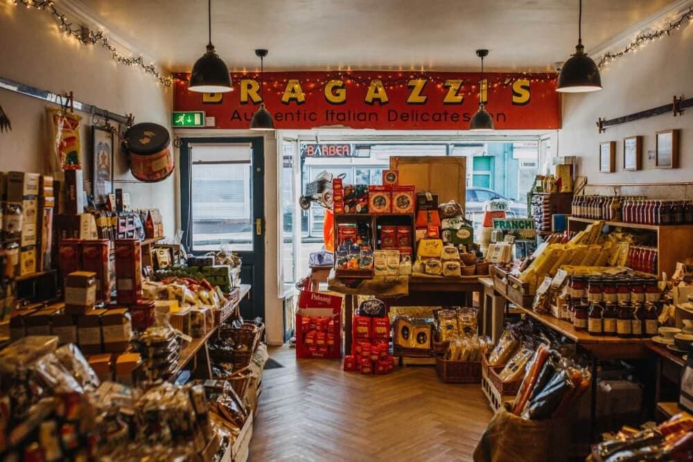 Cozy Italian delicatessen with shelves full of various food products and a vibrant red sign reading "RAGAZZI'S. - Home Instead
