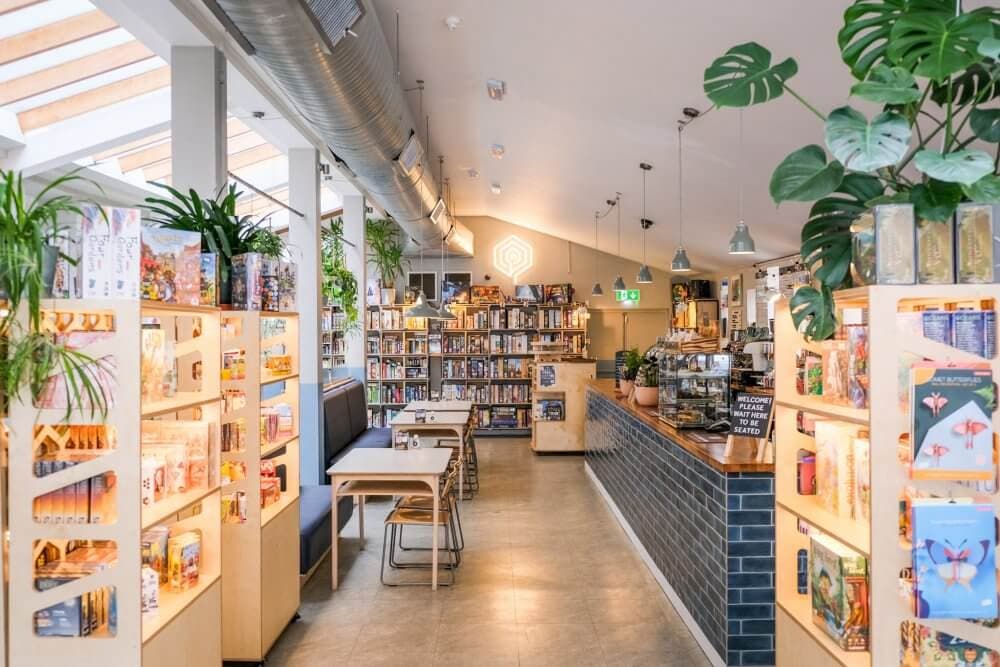 Bright modern bookstore with cozy seating, shelves full of books and games, and a small cafe counter on the right. - Home Instead