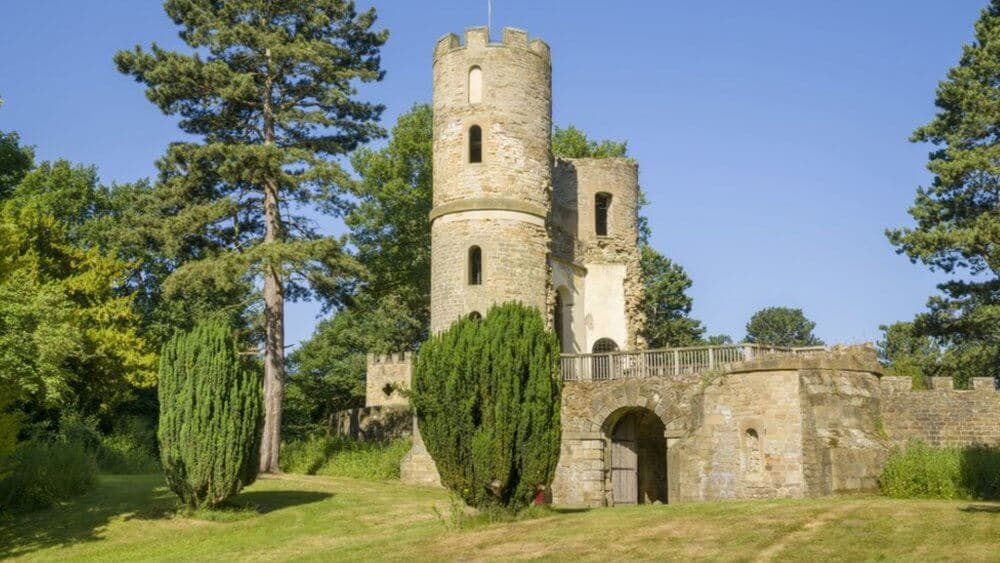 A round stone tower with an arched entrance, surrounded by trees and greenery under a clear blue sky. - Home Instead