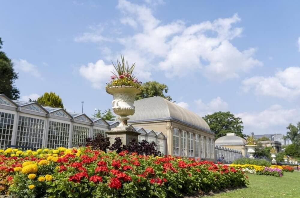 A beautiful garden with vibrant flowers and a large white conservatory building under a clear blue sky. - Home Instead