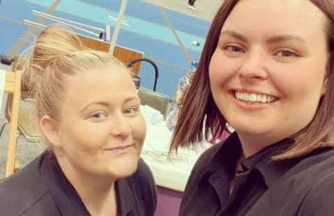 Two smiling women take a selfie together in an indoor setting, with sports equipment visible in the background. - Home Instead