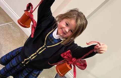 Young girl smiling, holding up two orange containers with red ribbons, dressed in a blue plaid dress and black cardigan. - Home Instead