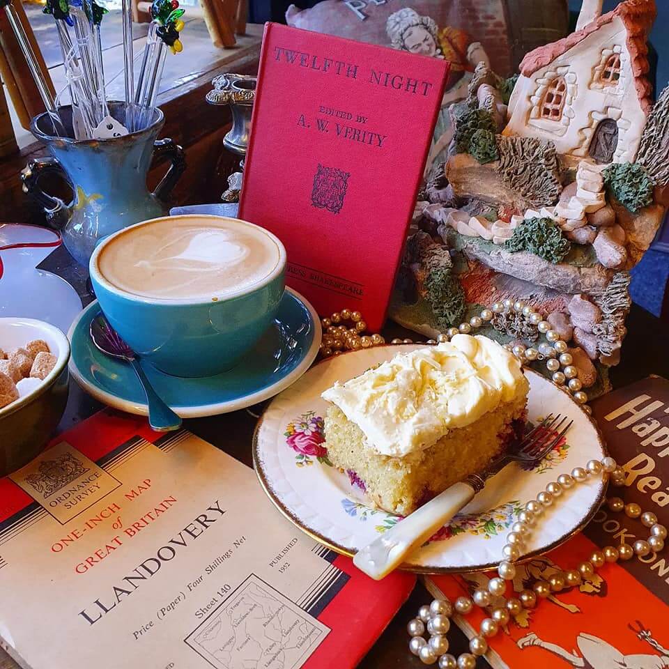 A coffee cup, a book, a slice of cake on a plate, a pearl necklace, a cottage model, and a map on a cluttered table. - Home Instead