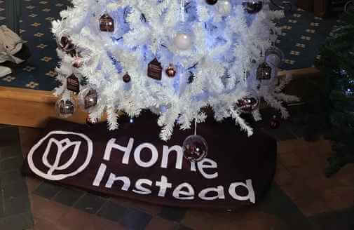 White Christmas tree with ornaments and the words "Home Instead" on a mat beneath the tree. - Home Instead