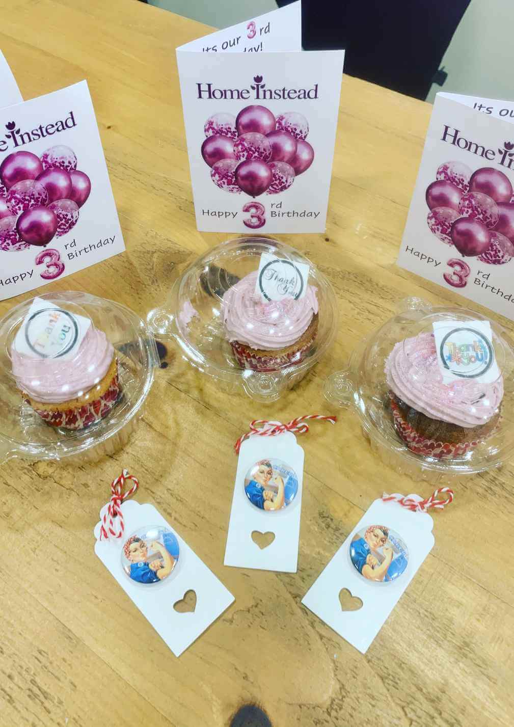 Three cupcakes in plastic containers, each with a card and tag with character stickers, celebrating a 3rd birthday. - Home Instead