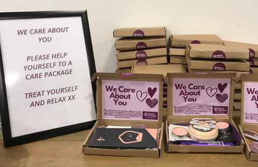 Care packages displayed on a table next to a sign reading, "We care about you. Please help yourself to a care package. - Home Instead
