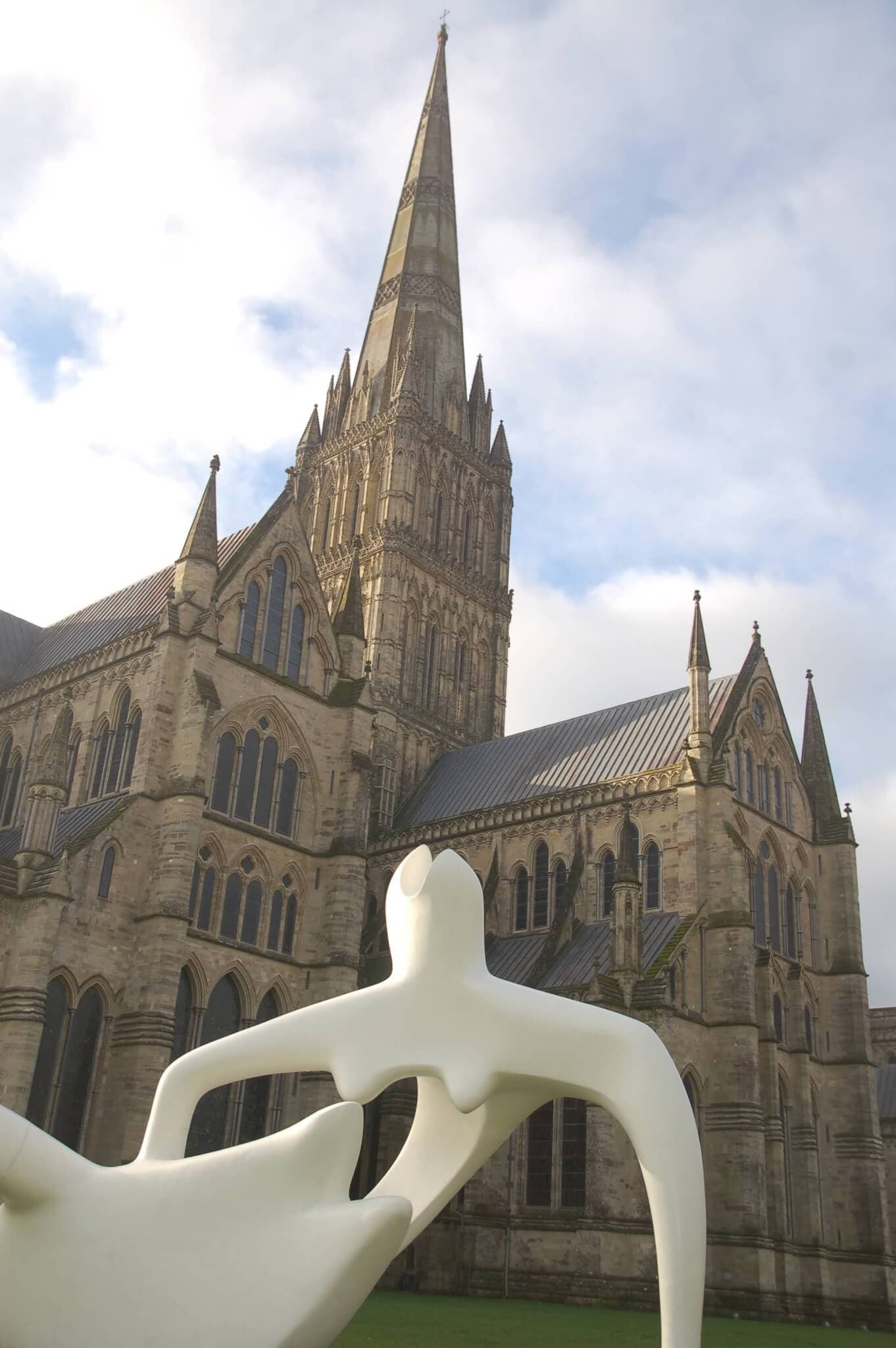 Abstract white sculpture in front of a large Gothic cathedral with a tall spire under a cloudy sky. - Home Instead