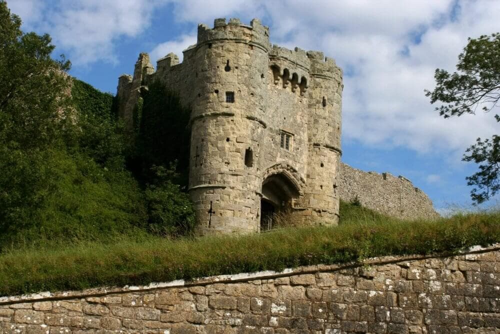 A historic stone castle with a fortified tower and arched entrance, surrounded by greenery and a partly cloudy sky. - Home Instead