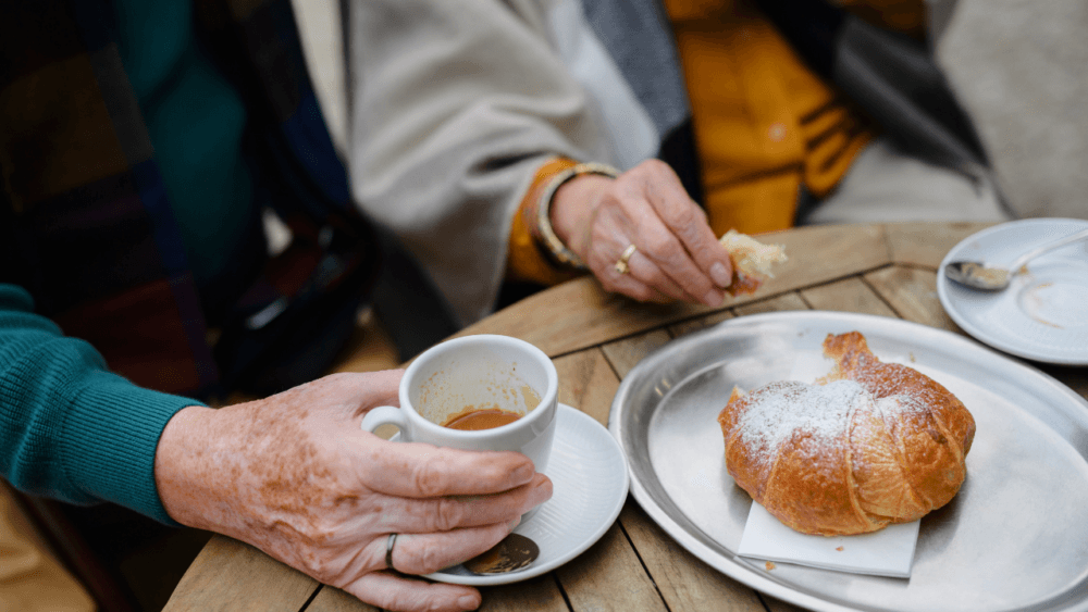 An elderly person enjoying a coffee and croissant at a cafe in Winchester - Home Instead Central Hampshire