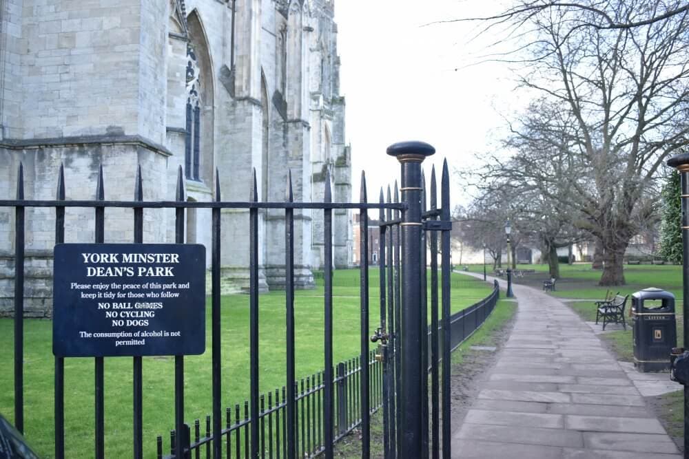 A walkway with a black wrought-iron gate and warning sign leading to York Minster Dean's Park. - Home Instead