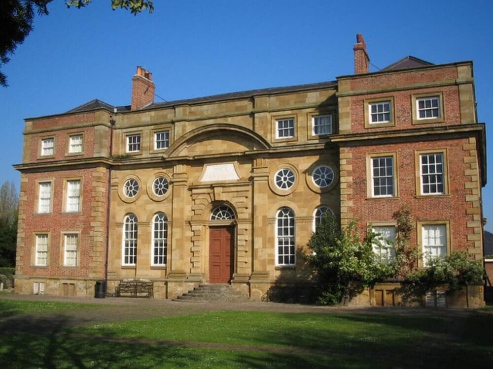 Historic red-brick and stone building with large windows and an arched doorway, set against a clear blue sky. - Home Instead
