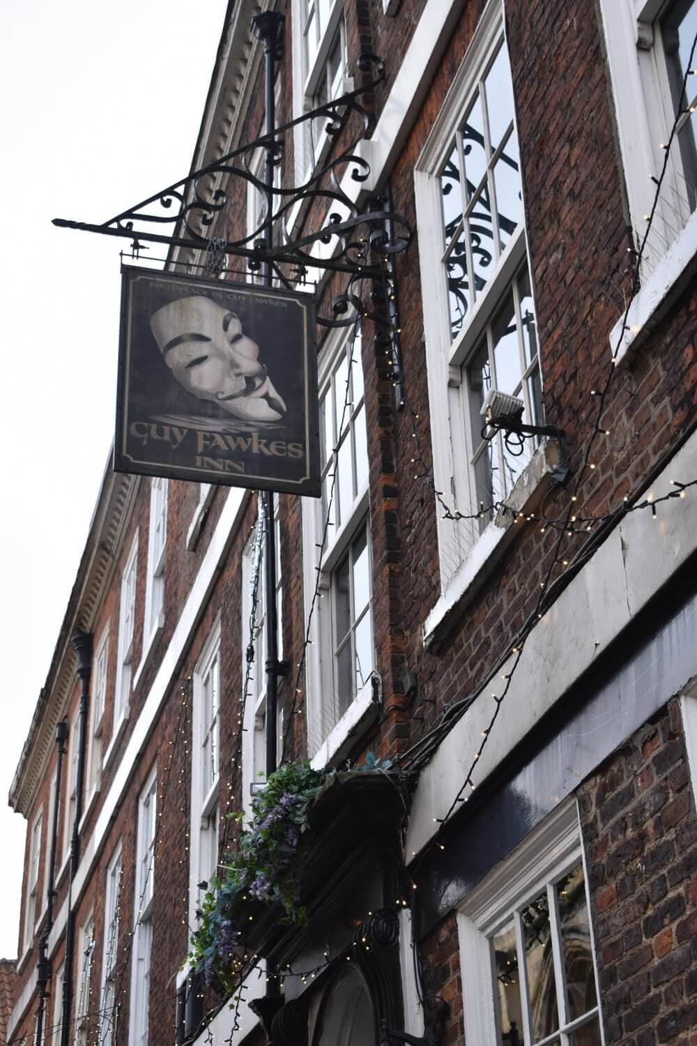An old brick building with a "Guy Fawkes Inn" sign and string lights hanging outside. - Home Instead