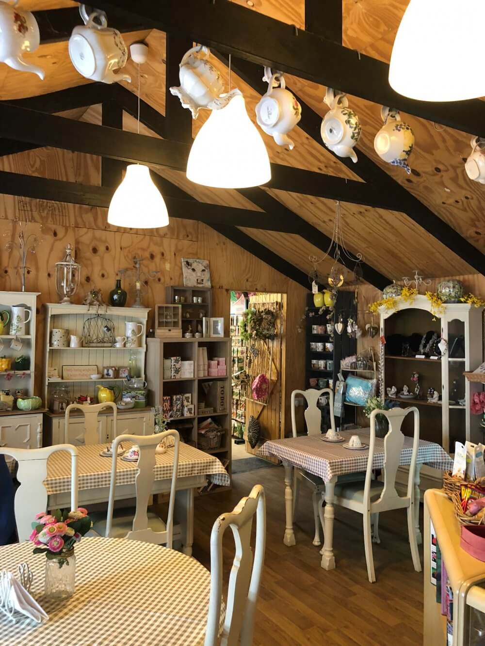 Cozy café with gingham-covered tables, elegant white chairs, and shelves displaying various teapots and decor. - Home Instead