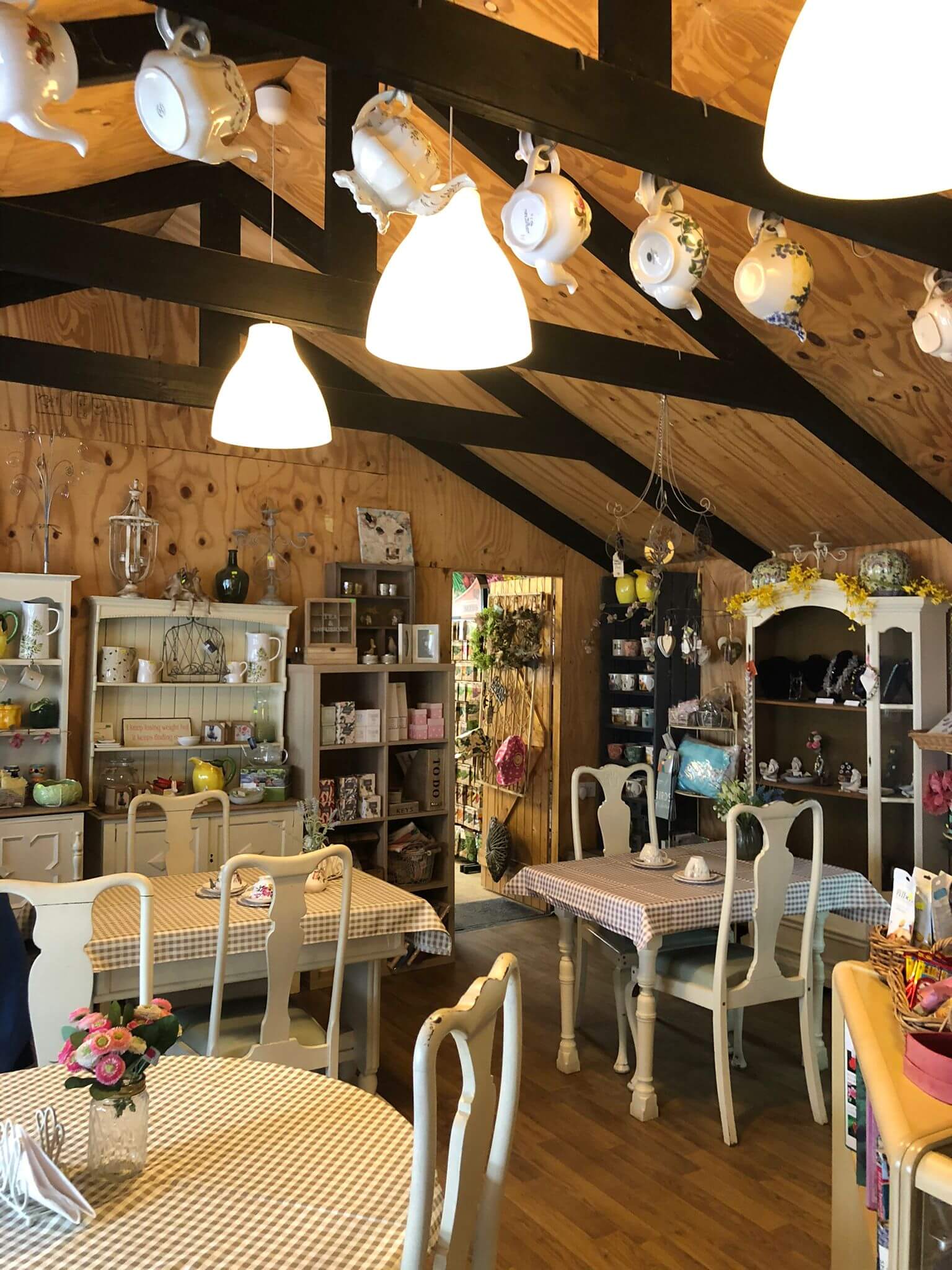 Cozy café with gingham-covered tables, elegant white chairs, and shelves displaying various teapots and decor. - Home Instead