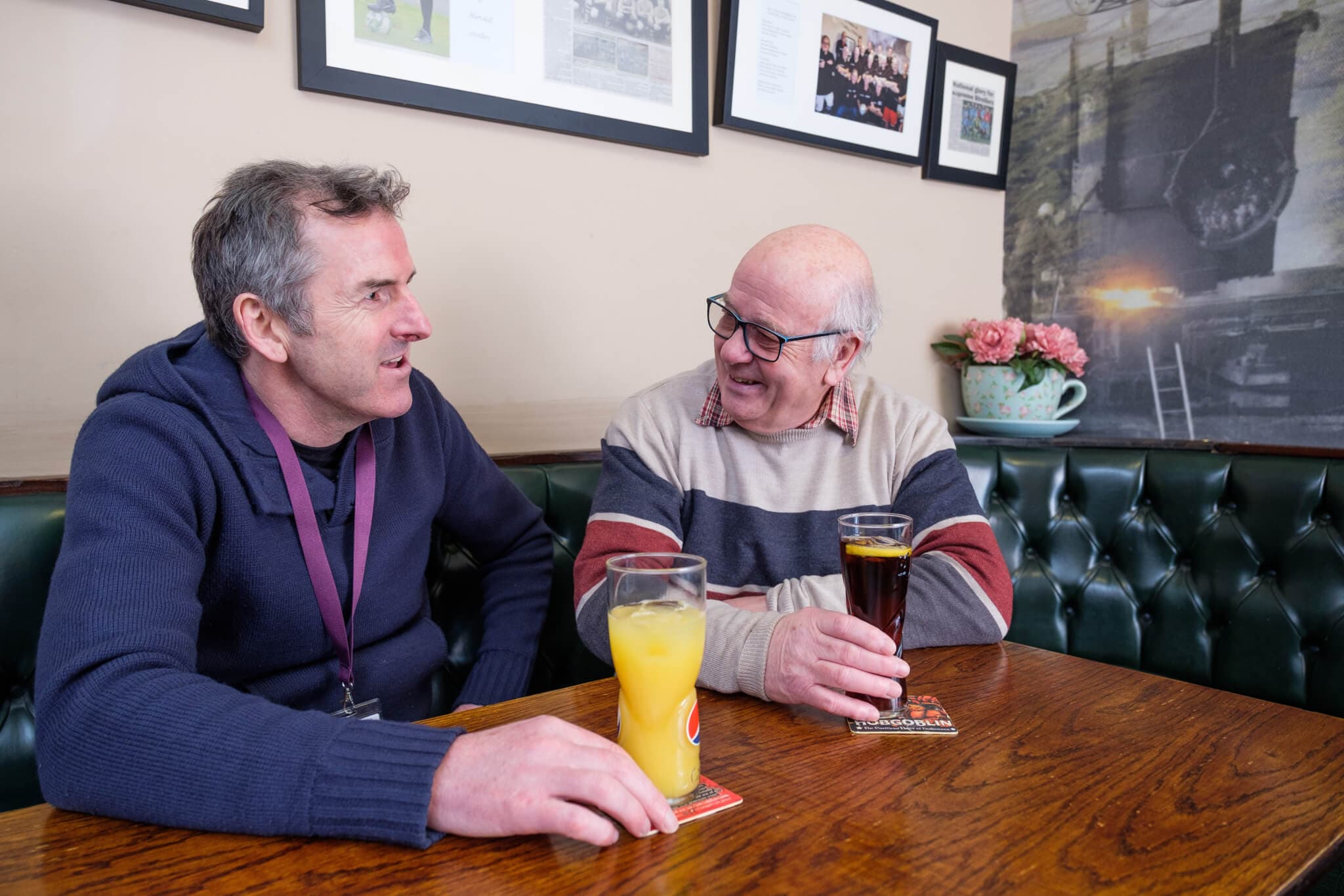 Two men enjoying drinks at a pub, sitting across from each other at a wooden table, engaging in conversation. - Home Instead