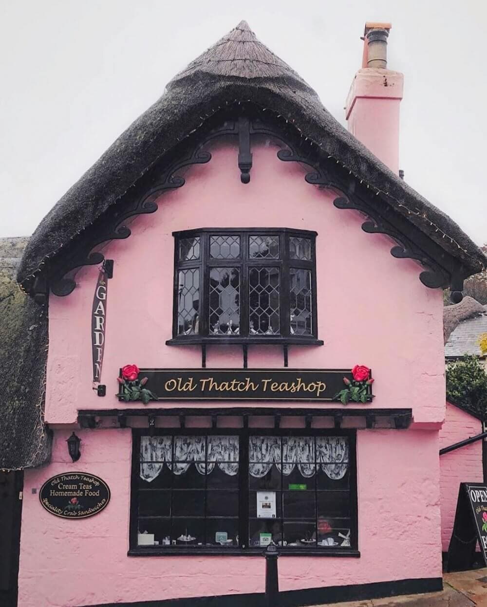 Charming pink thatched-roof teashop with a sign that reads "Old Thatch Teashop" and a window display. - Home Instead