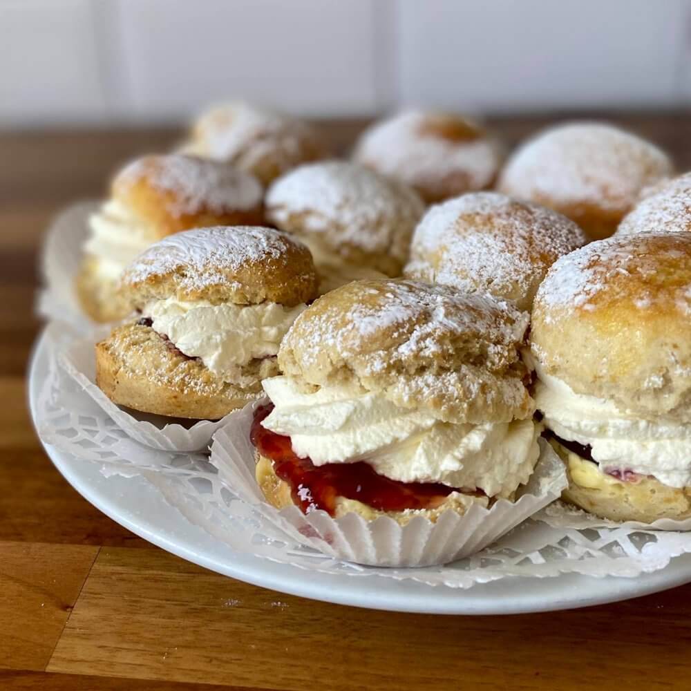 A plate of scones filled with cream and jam, dusted with powdered sugar, served on a wooden table. - Home Instead