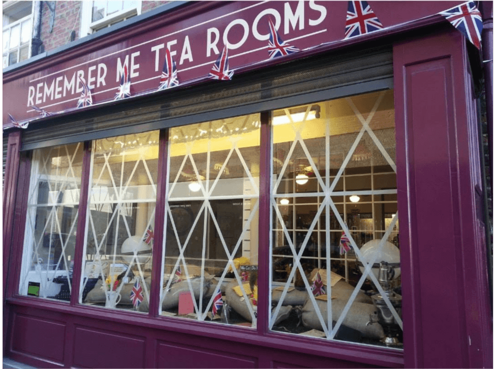 A tea room with a maroon exterior named "Remember Me Tea Rooms" adorned with Union Jack flags. - Home Instead