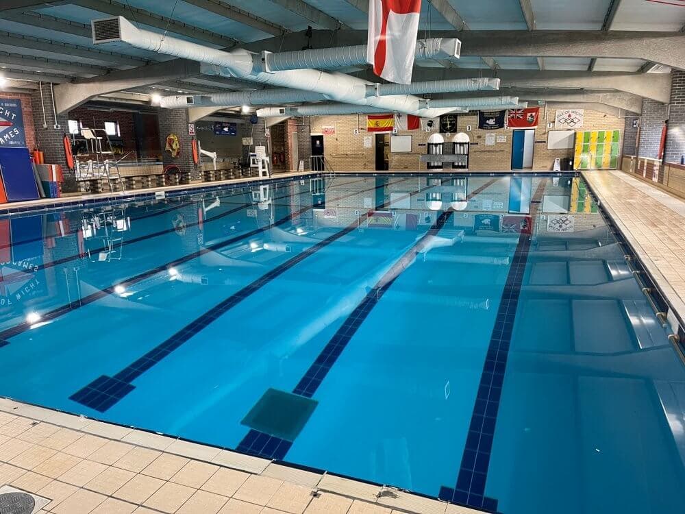 An indoor swimming pool with blue lanes and flags hanging from the ceiling. The pool area is brightly lit. - Home Instead