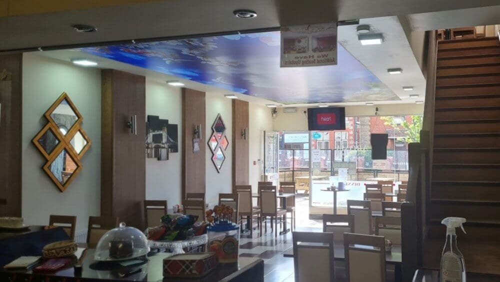 A brightly lit restaurant interior with wooden tables, chairs, decorative mirrors, and a counter with various items. - Home Instead